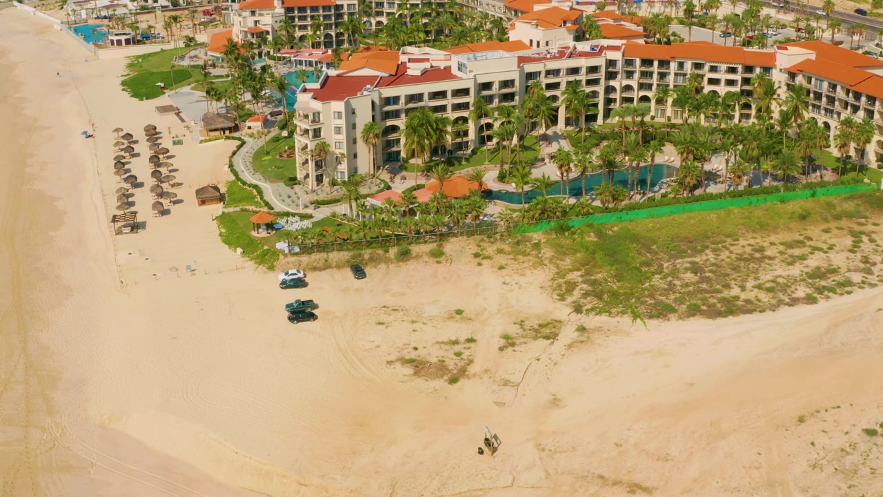 At 0:02, the Dreams Beach aerial frame shows hotel wings stretching across the top, palm-lined pool grounds in the center, broad sand in front, and no visible people.