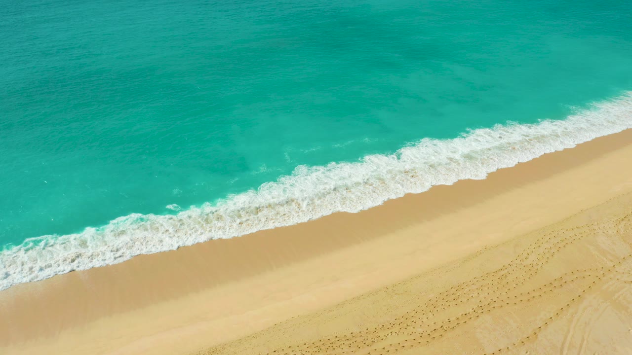 Overhead view of turquoise water rolling onto pale sand at Dreams Beach, Baja California Sur, Mexico, with dotted sand marks near the lower edge and no visible people.