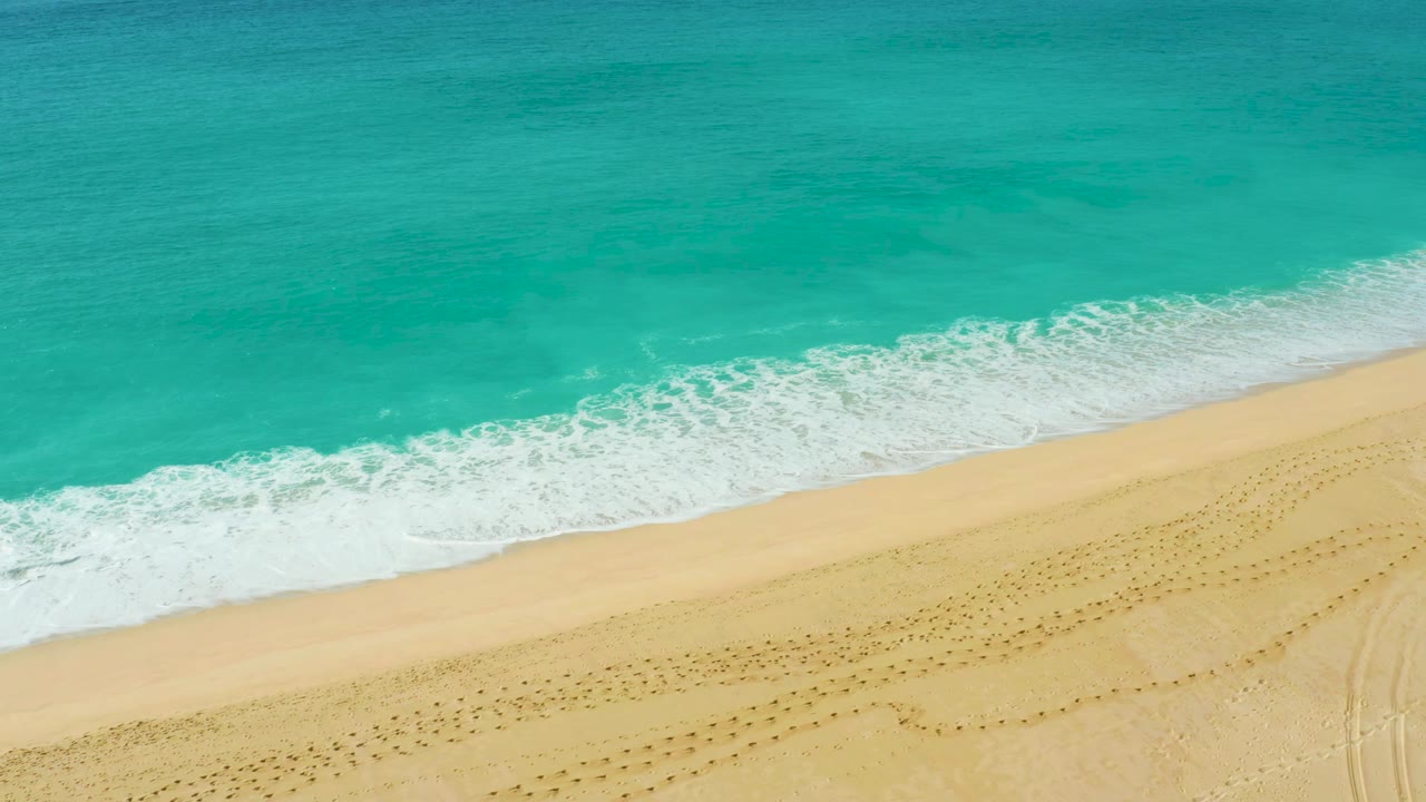 Aerial shoreline frame at Dreams Beach in Baja California Sur with a wider band of white foam sliding across the wet sand and no visible people.