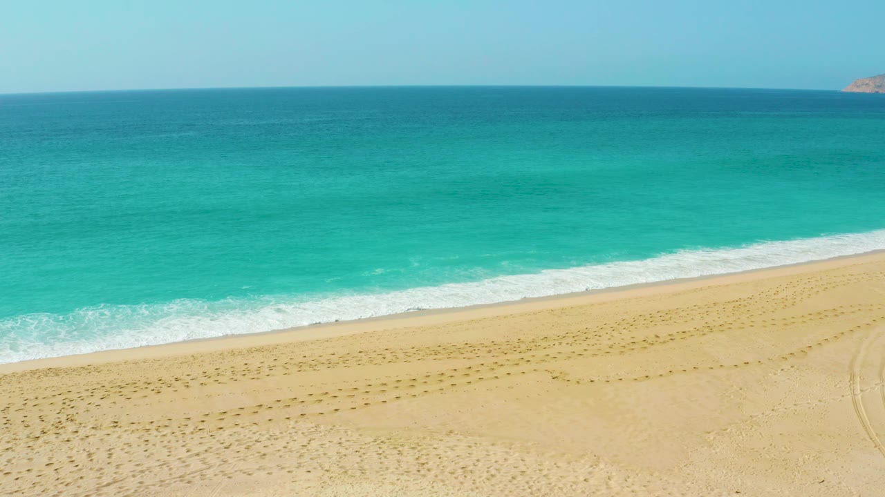 Dreams Beach shoreline from an elevated angle, with the ocean occupying the upper frame, a foamy wave band crossing the beach, and no visible people.