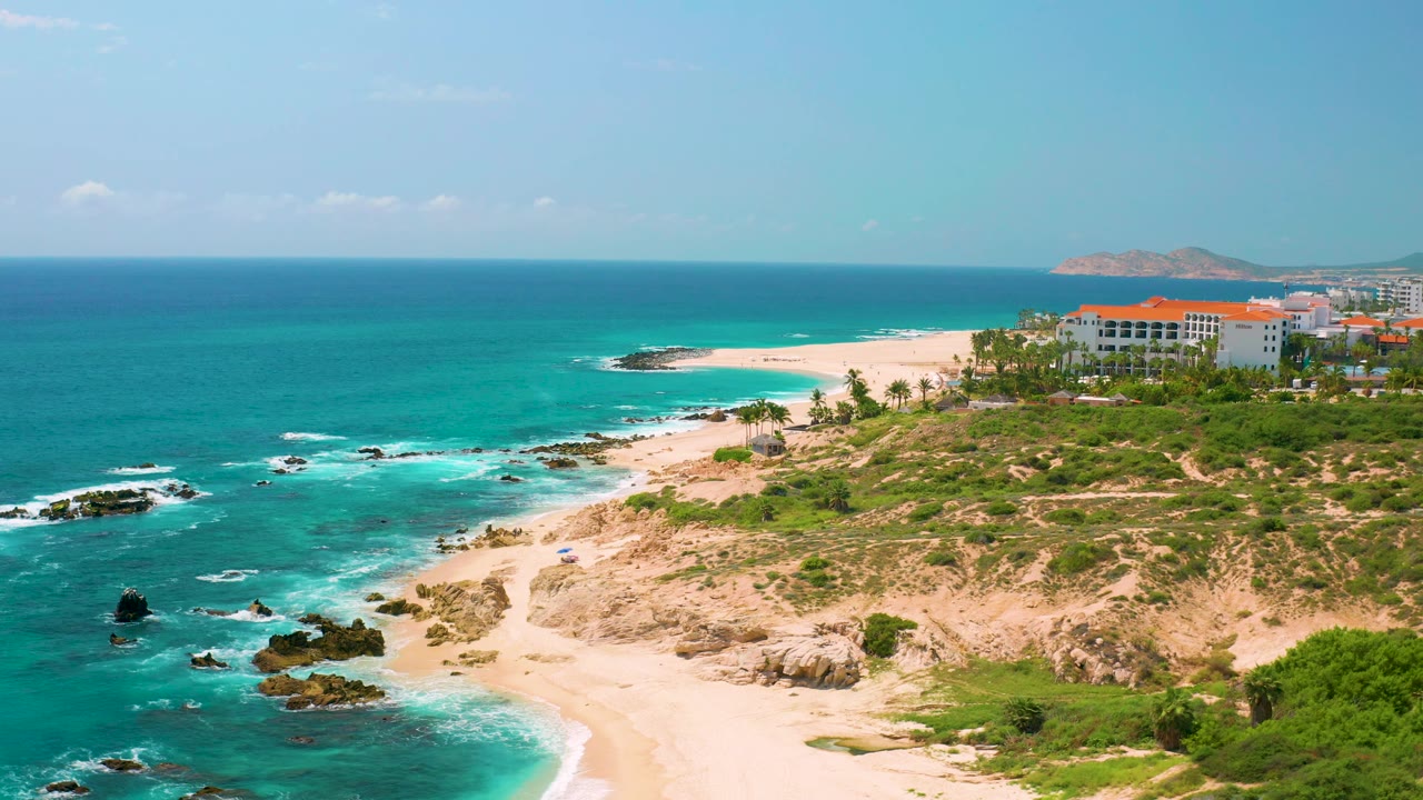 Aerial beach landscape with rocks in turquoise water and a distant headland.