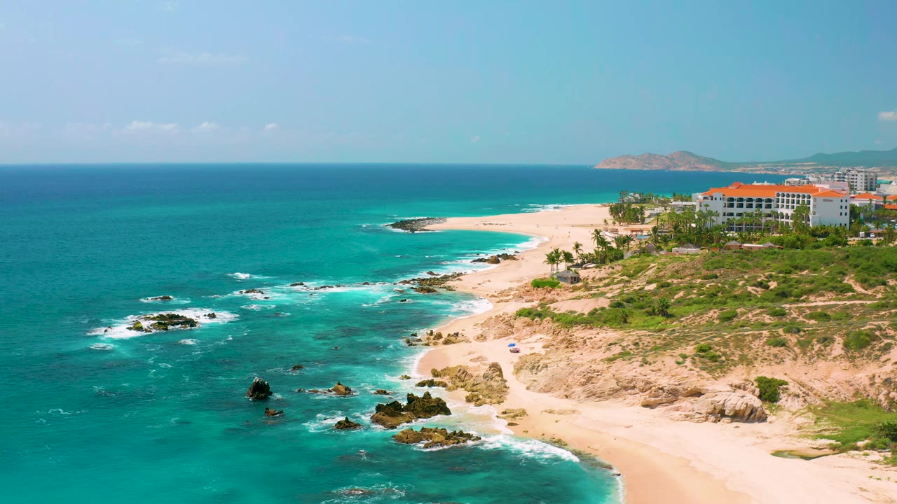 Turquoise water beside a white beach with rocks and red-roofed buildings