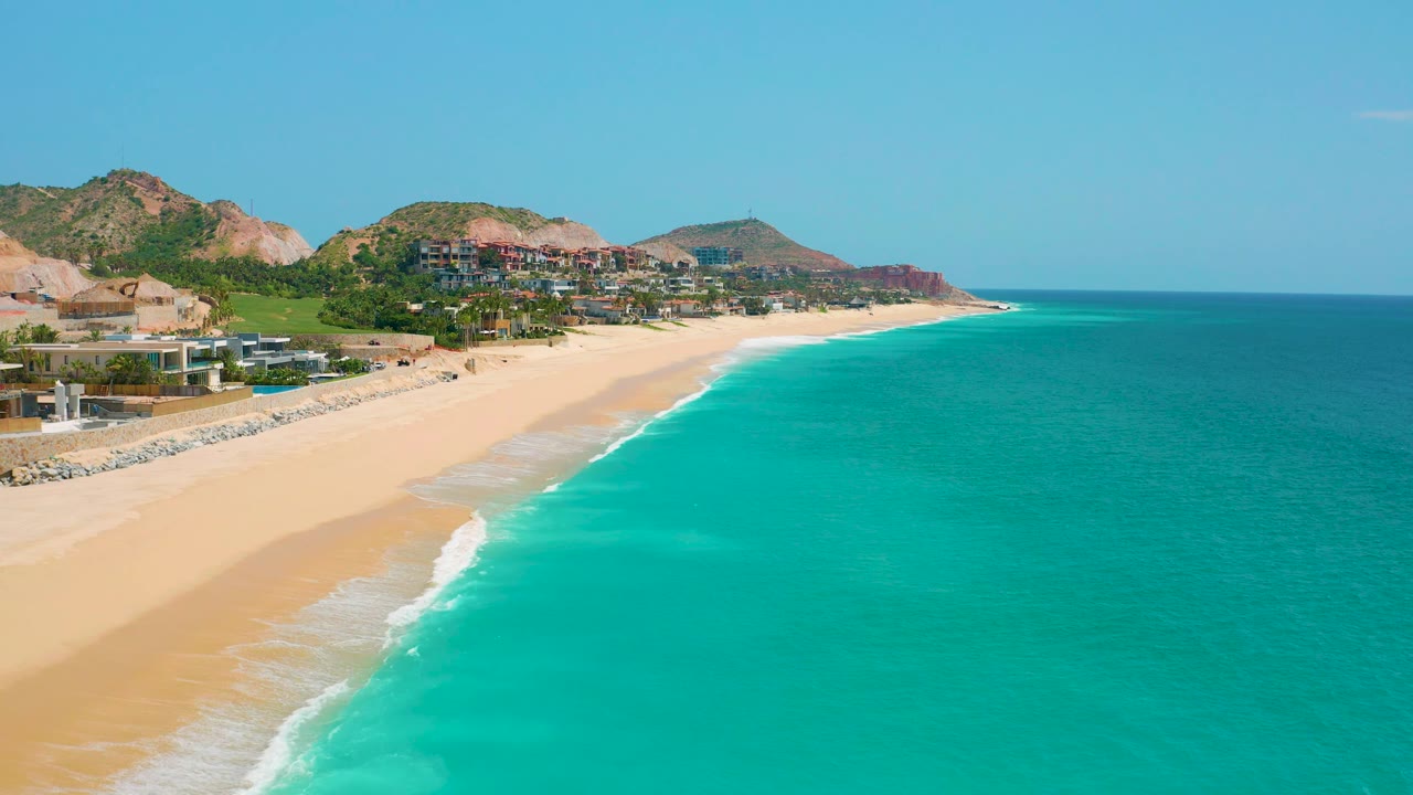 Sandy beach, gentle surf, ocean, hills, and buildings from a high coastal angle.