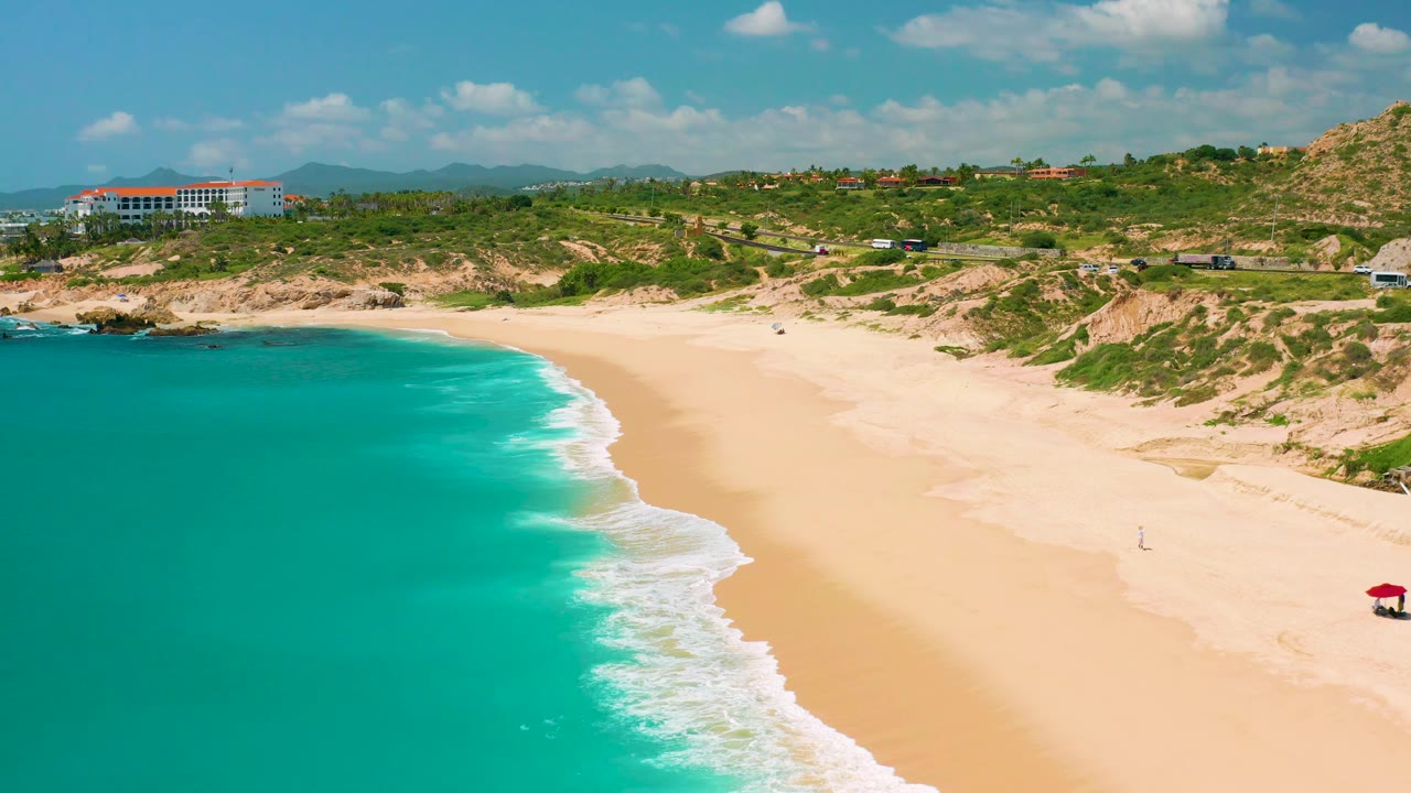 High beach view with bright turquoise water, foamy shore break, and hillside buildings.