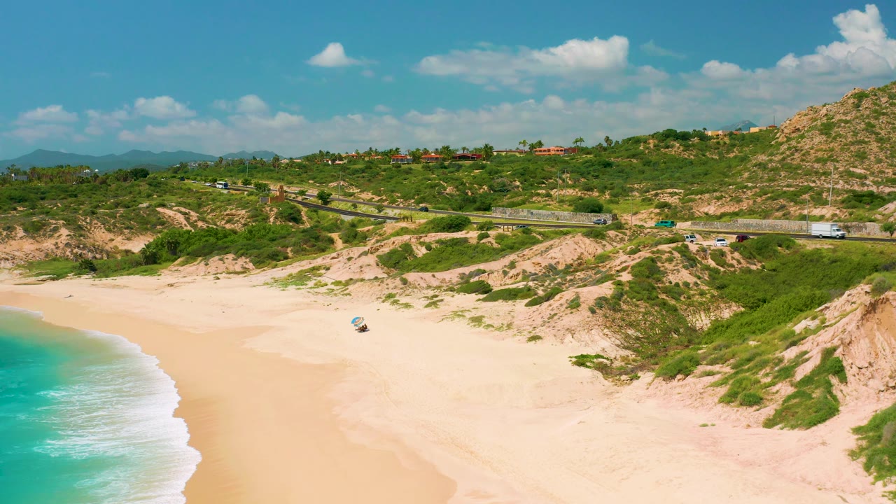 High coastal view with surf, open beach, scrub dunes, road, and hills