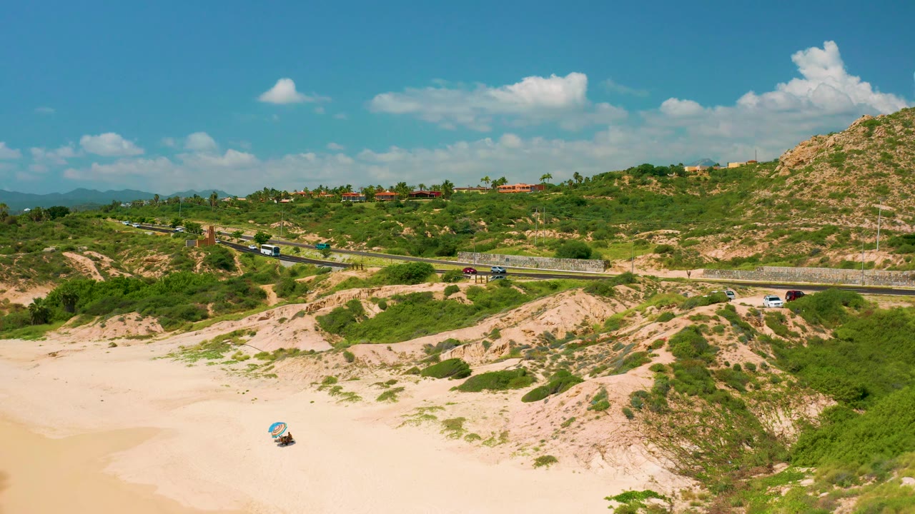 Aerial beach foreground with cars moving along a hillside highway