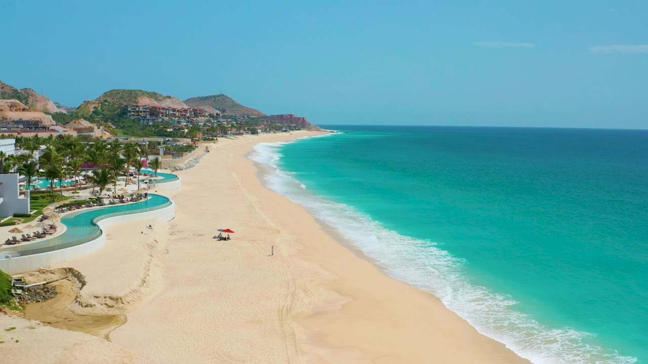 Aerial coastline with resort pool foreground, sandy beach, and turquoise surf.