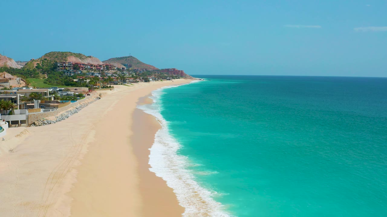 Dreams Beach appears from above with a broad turquoise ocean field on the right, a pale sand curve on the left, hillside development, and no visible people.