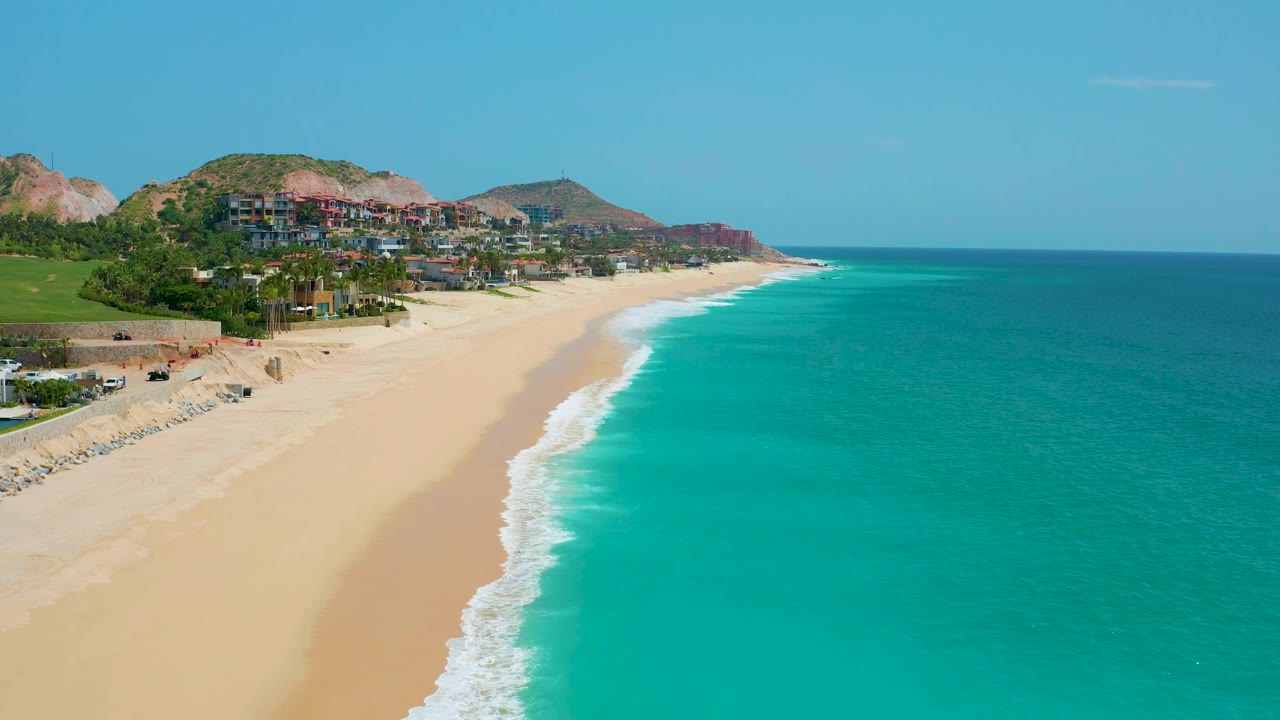 At 0:02, the shoreline curve is visible from above at Dreams Beach, Baja California Sur, Mexico, with surf foam on the sand and no visible people.