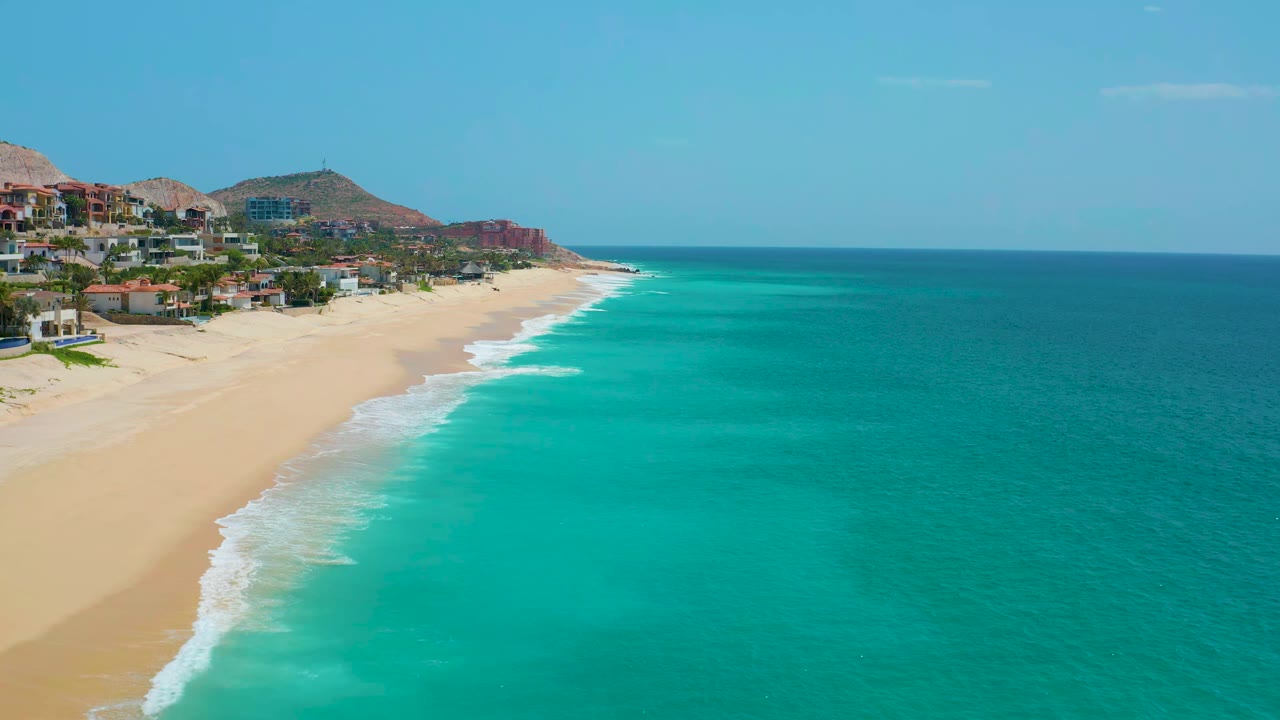 Turquoise waves angle along a sandy beach below hillside homes.