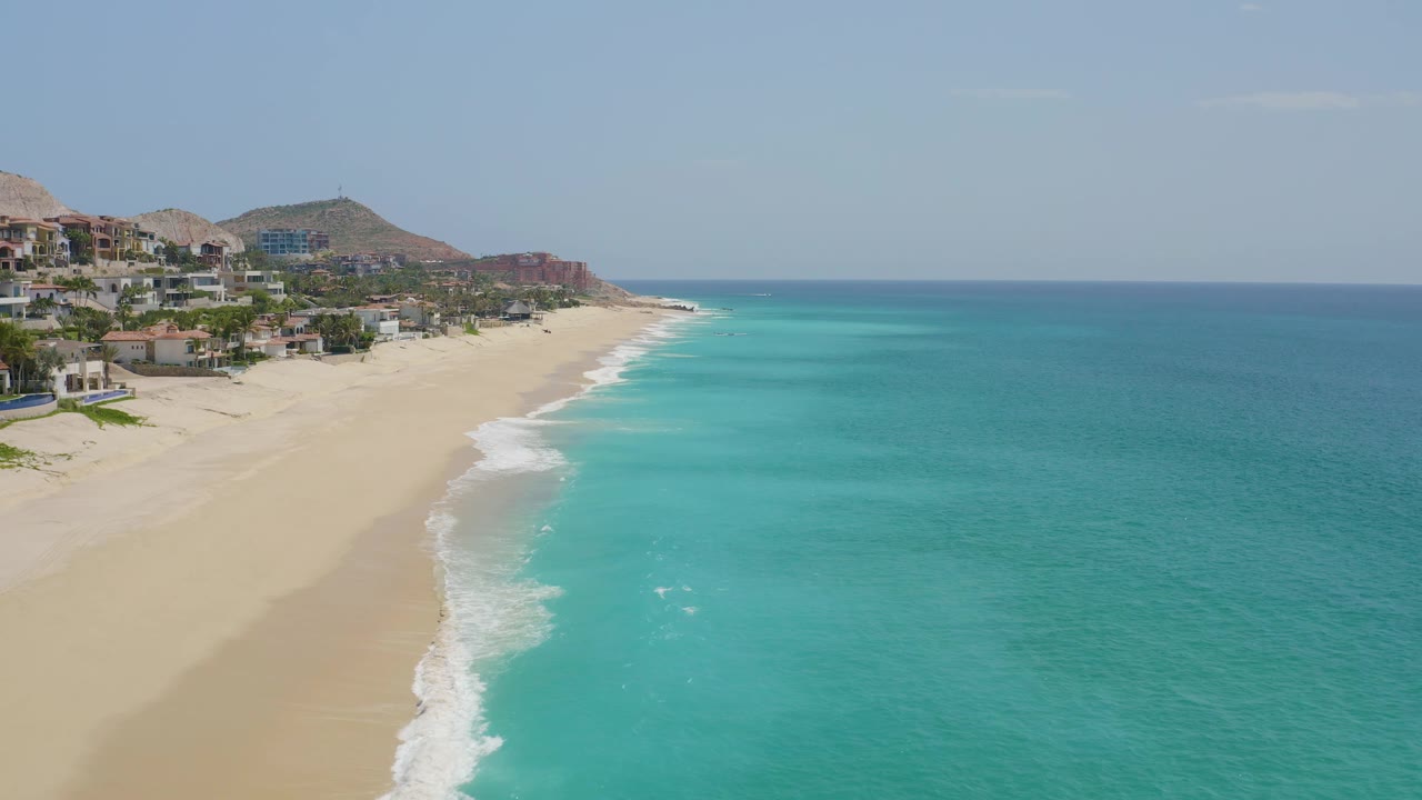 Elevated view over Dreams Beach as the foamy water line curves along the sand, with open blue ocean filling the right side and no visible people on the beach.