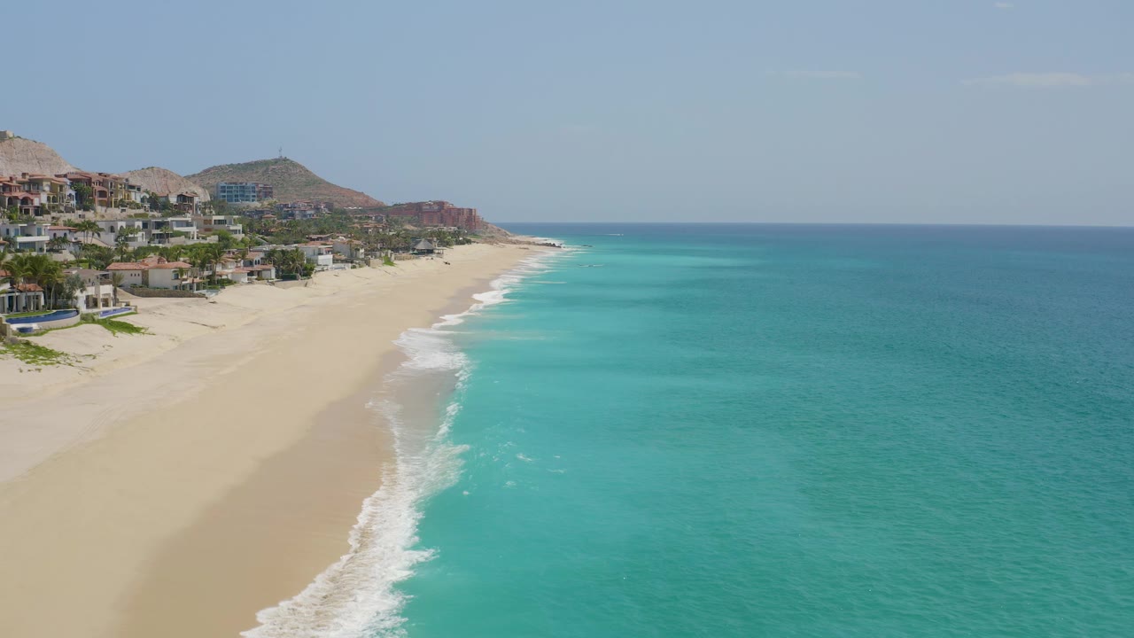 Aerial coastline view with hillside buildings and surf line.