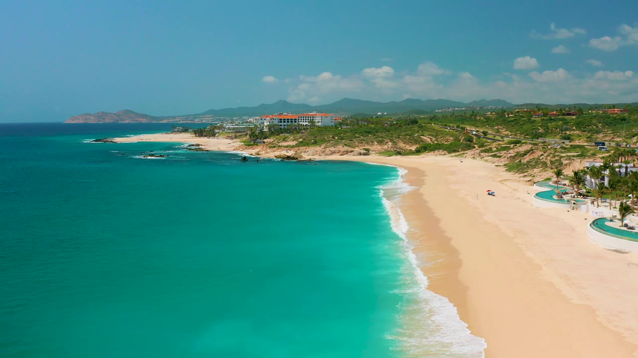 High aerial frame at Dreams Beach in Baja California Sur, Mexico, with the ocean covering most of the left side, the beach running diagonally, and no visible people.