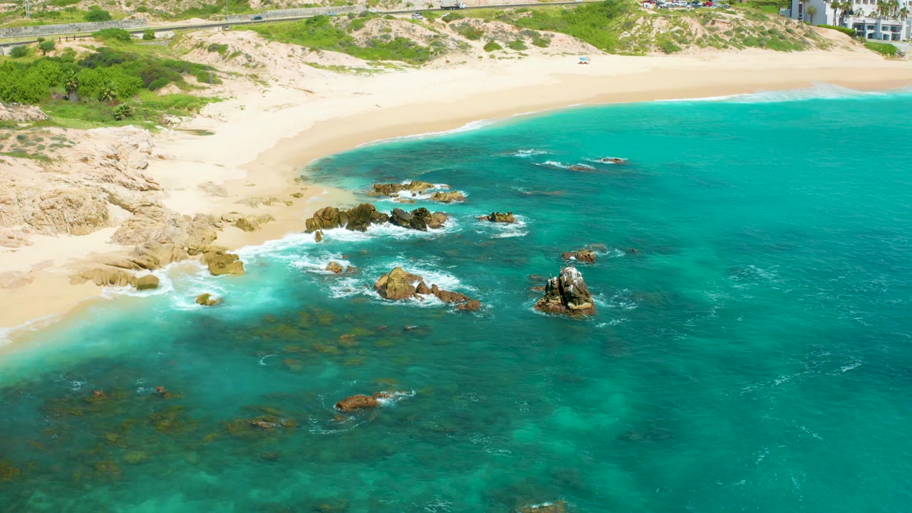 Rocky beach cove with blue-green water and waves breaking near shore.