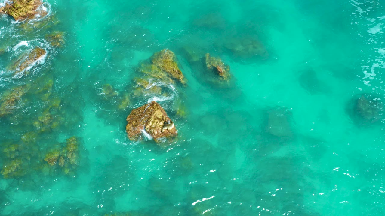 Turquoise water surrounding tan coastal rocks.