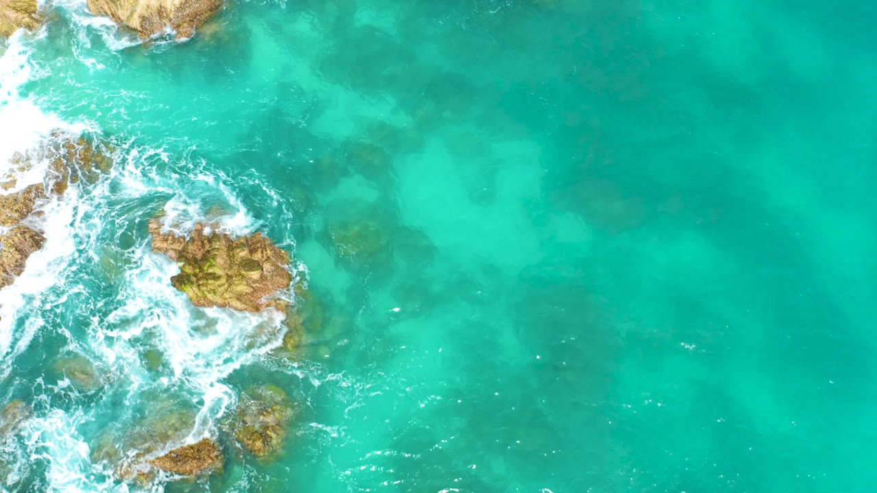 Rocky surf at the left edge with clear green water beside it.