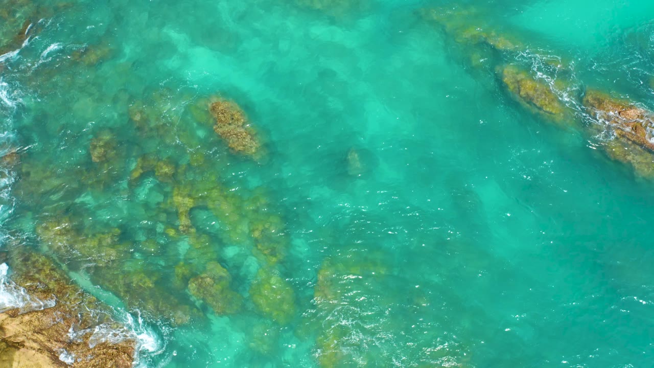 Turquoise water at Dreams Beach in Baja California Sur covers clustered rock shelves, with white surf tracing the lower-left and upper-right edges and no visible people.