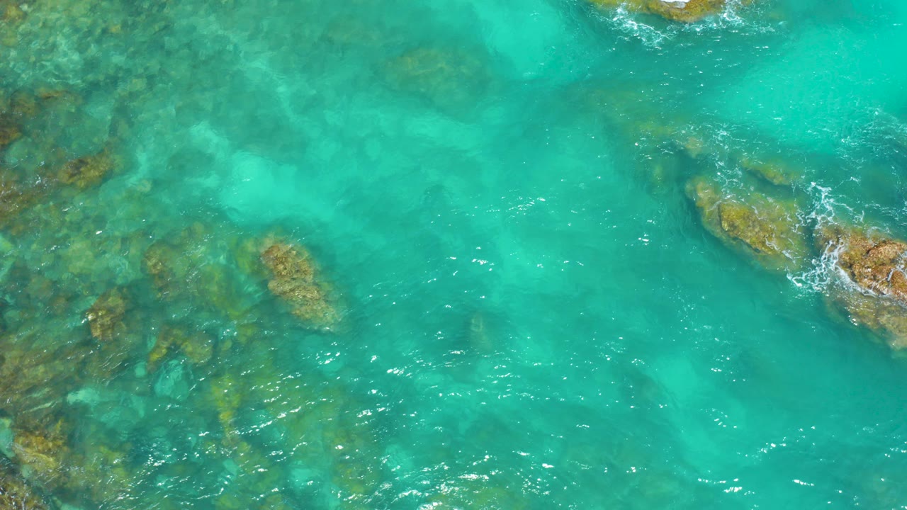 Overhead turquoise water with submerged rocks and small wave breaks.