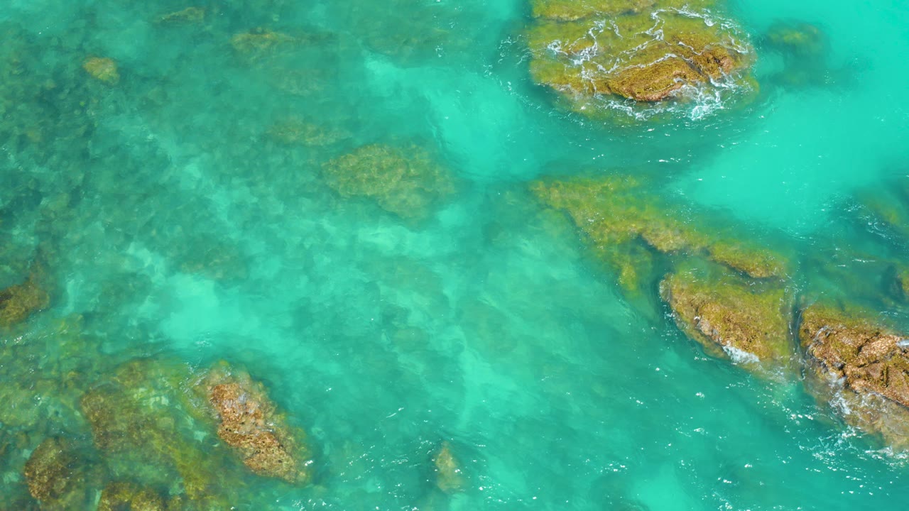 Overhead view of turquoise water and brown rock formations at Dreams Beach in Baja California Sur, Mexico, with small foam patches and no visible people.