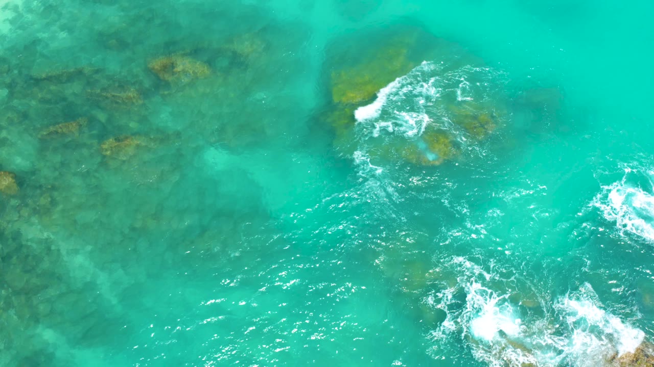 Clear turquoise sea over reef at Dreams Beach in Baja California Sur, with darker rock shapes on the left and white breaking water on the right, with no visible people.