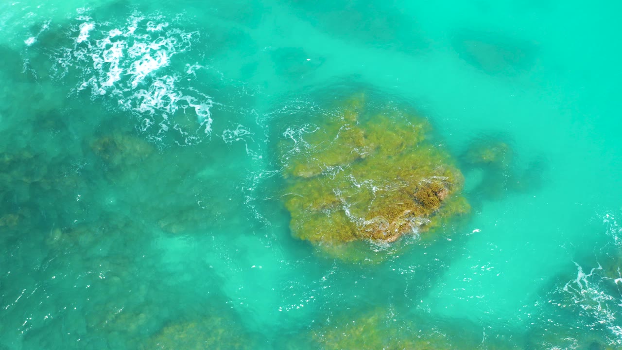 Turquoise water over submerged rocks with white foam at upper left.