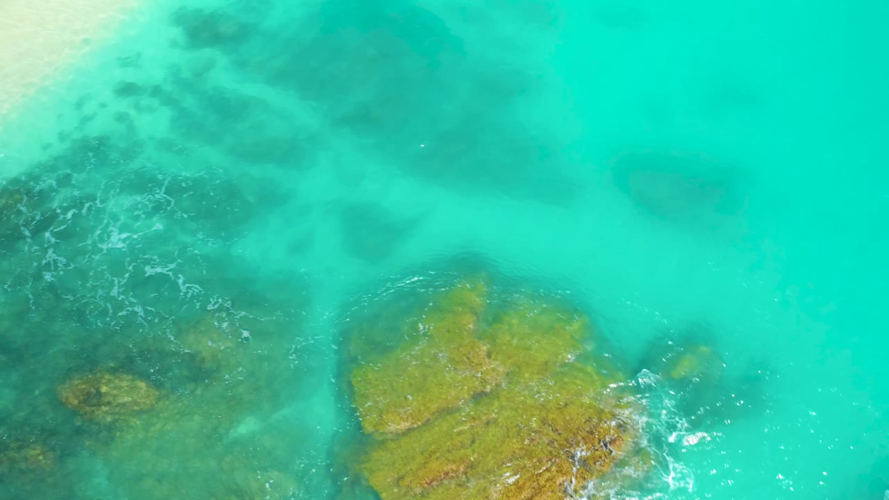 Clear blue water with submerged rocks and small wave foam