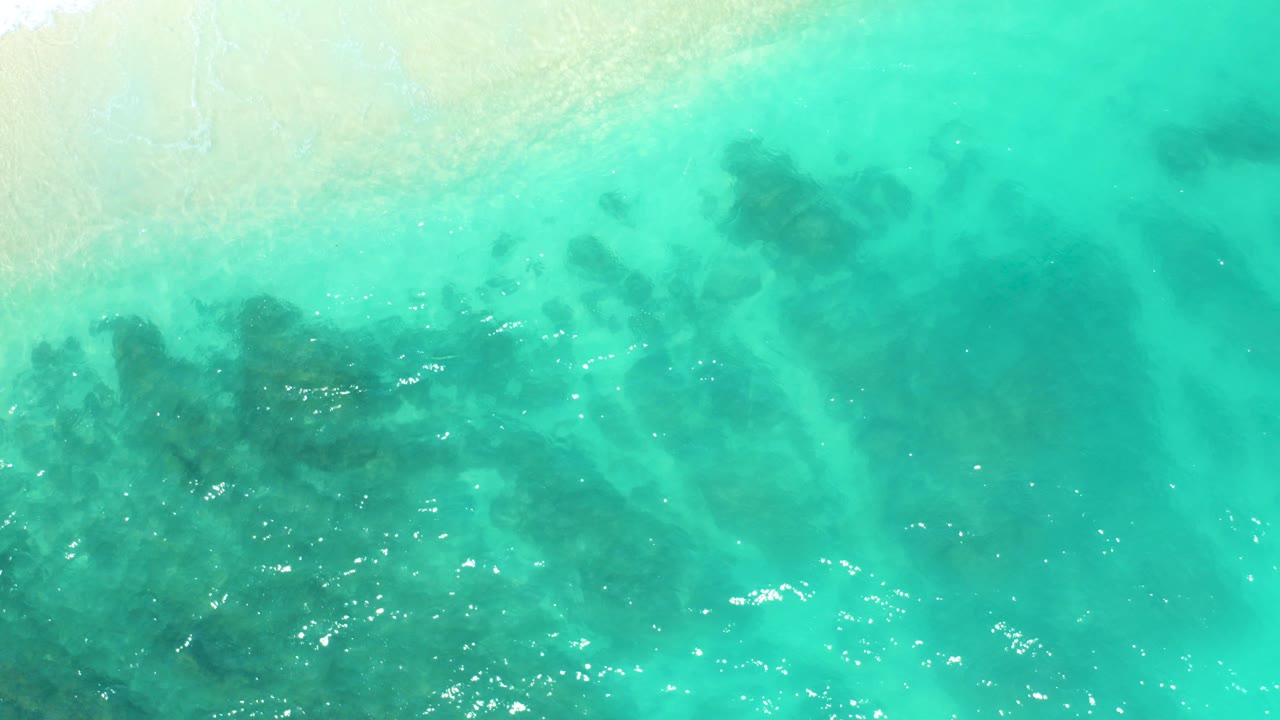 Turquoise shallow sea with dark submerged patches and pale sand at the top edge.