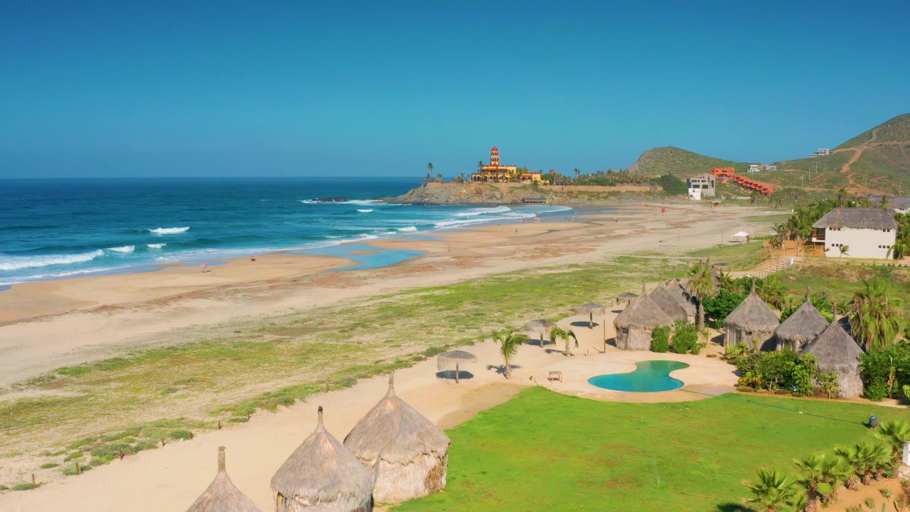 Elevated Cerritos, Baja California Sur view with clear sky, deep blue water, pale sand, resort huts, pool, and no visible people.