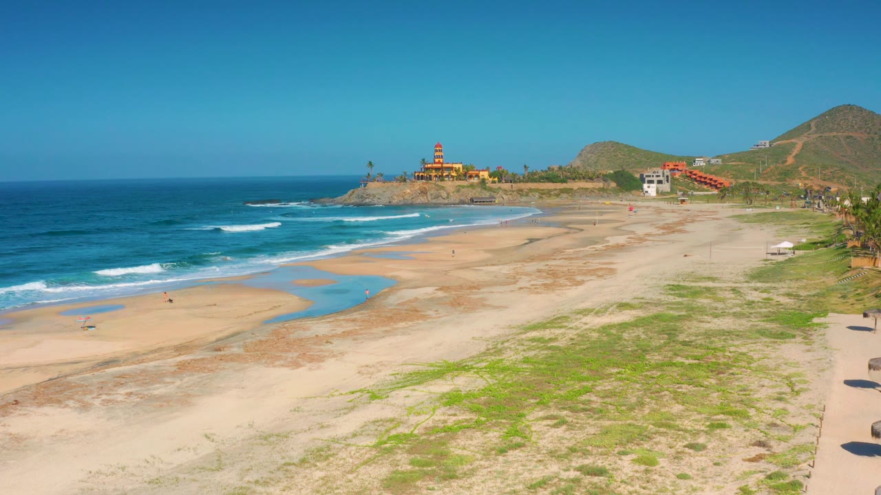 Elevated beach view with ocean on the left and a fort-like structure near the horizon.