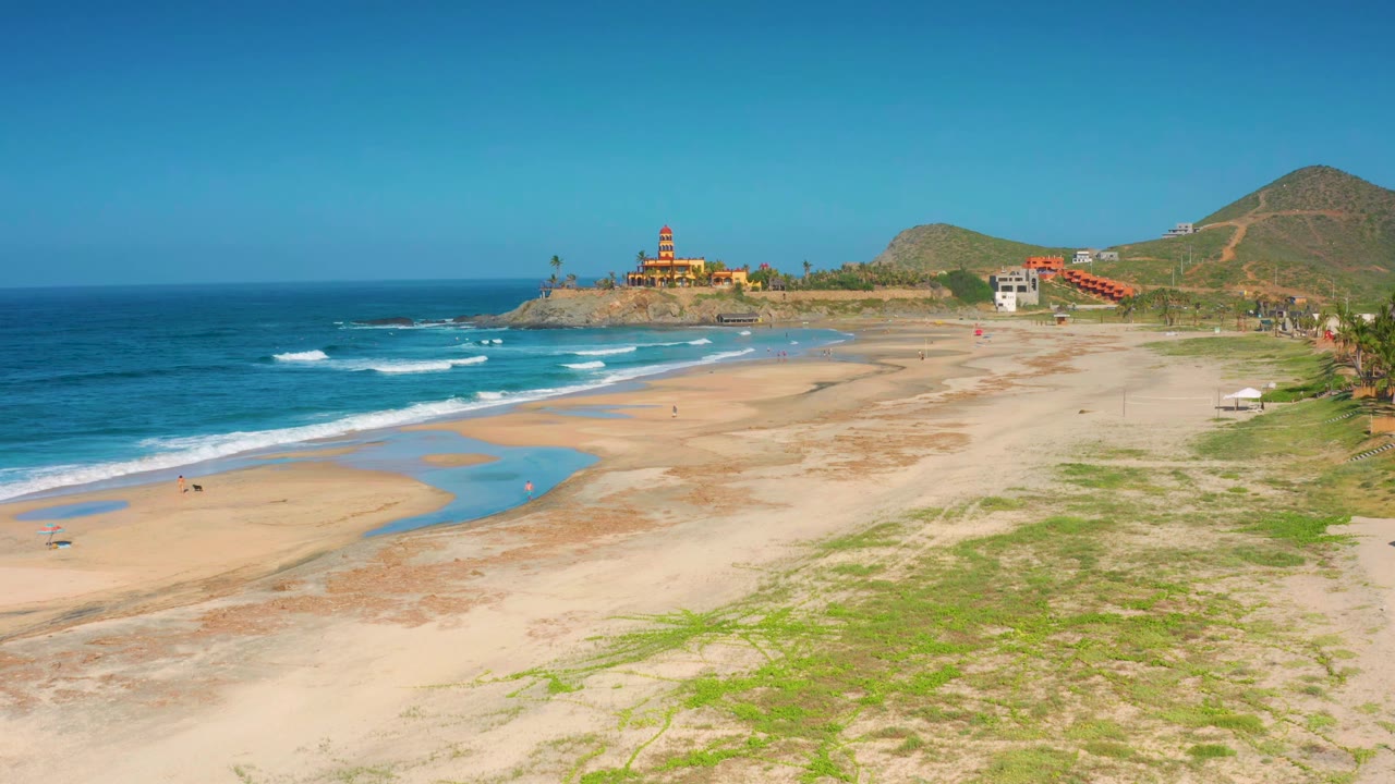 At 0:01, the Cerritos beach view holds wide with white wave bands closer to shore, bright shallow pools on the sand, hillside terrain in back, and no visible people identifiable.