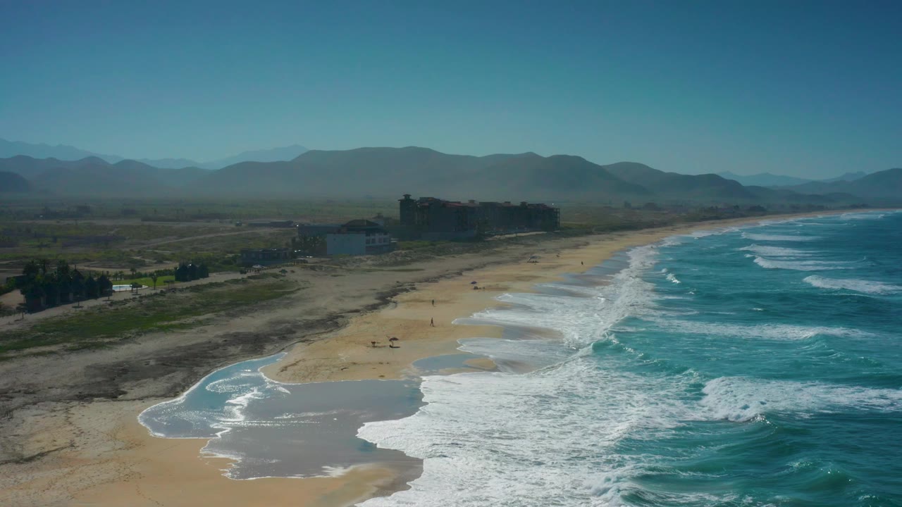 Aerial coastline with curved wet sand pools and surf beside a long beach.