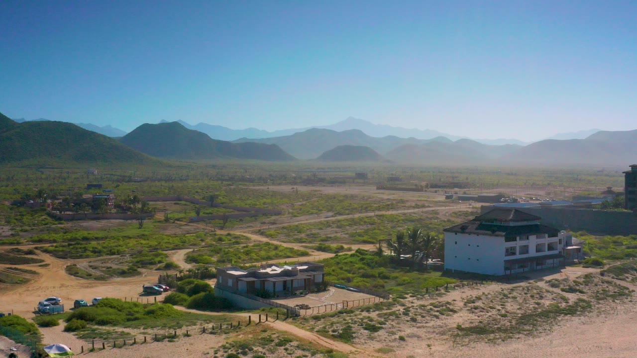 Elevated view in Cerritos, Baja California Sur showing scattered houses, sandy tracks, scrub vegetation, distant hazy mountains, and no visible people.