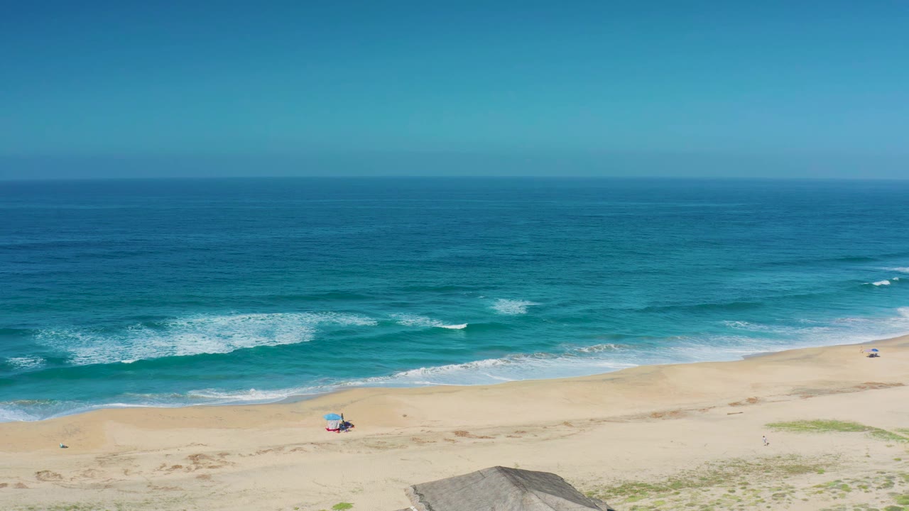 Turquoise waves roll toward a sandy beach with a small chair setup.