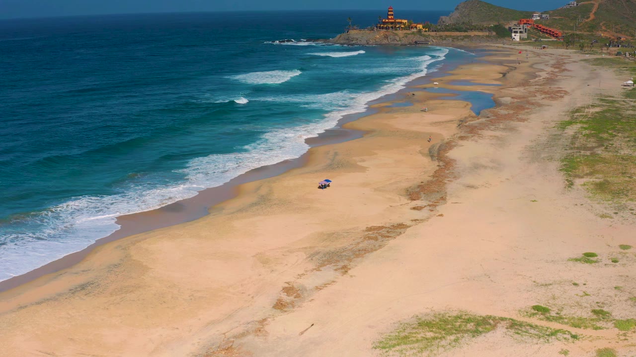 White surf lines approach a broad beach from a high coastal angle