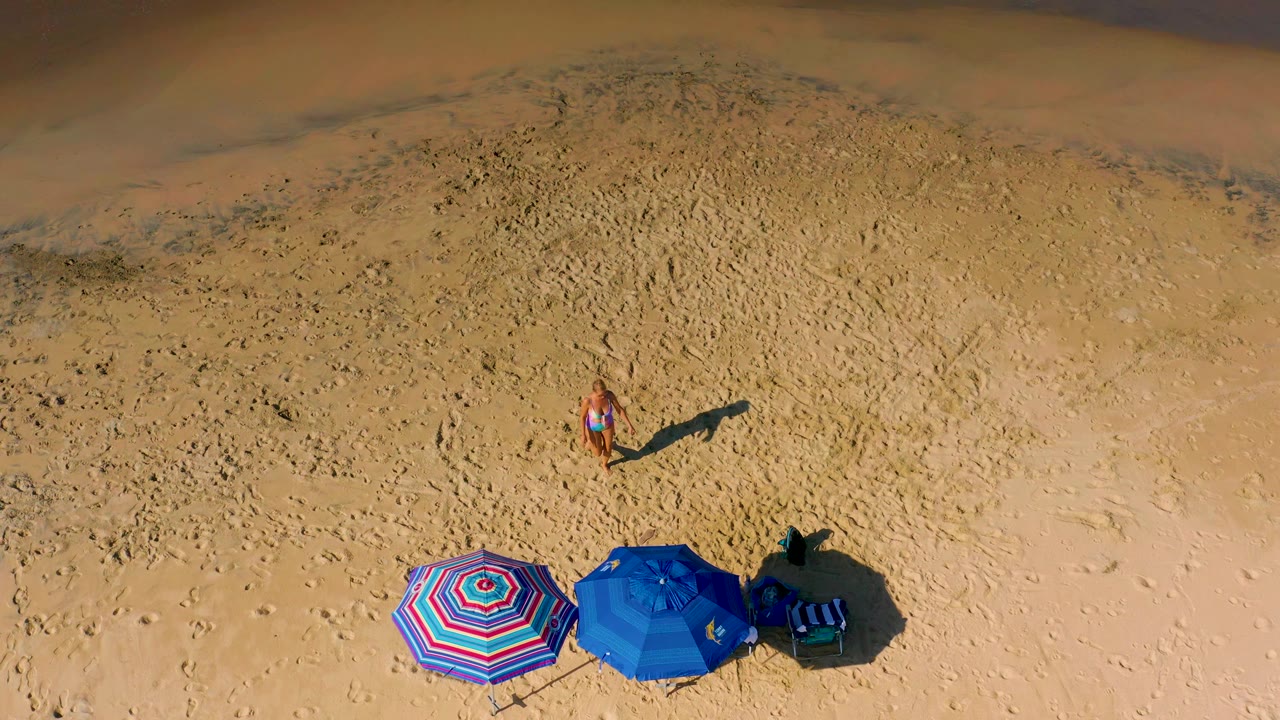 Overhead view of beach umbrellas and a woman on sand.