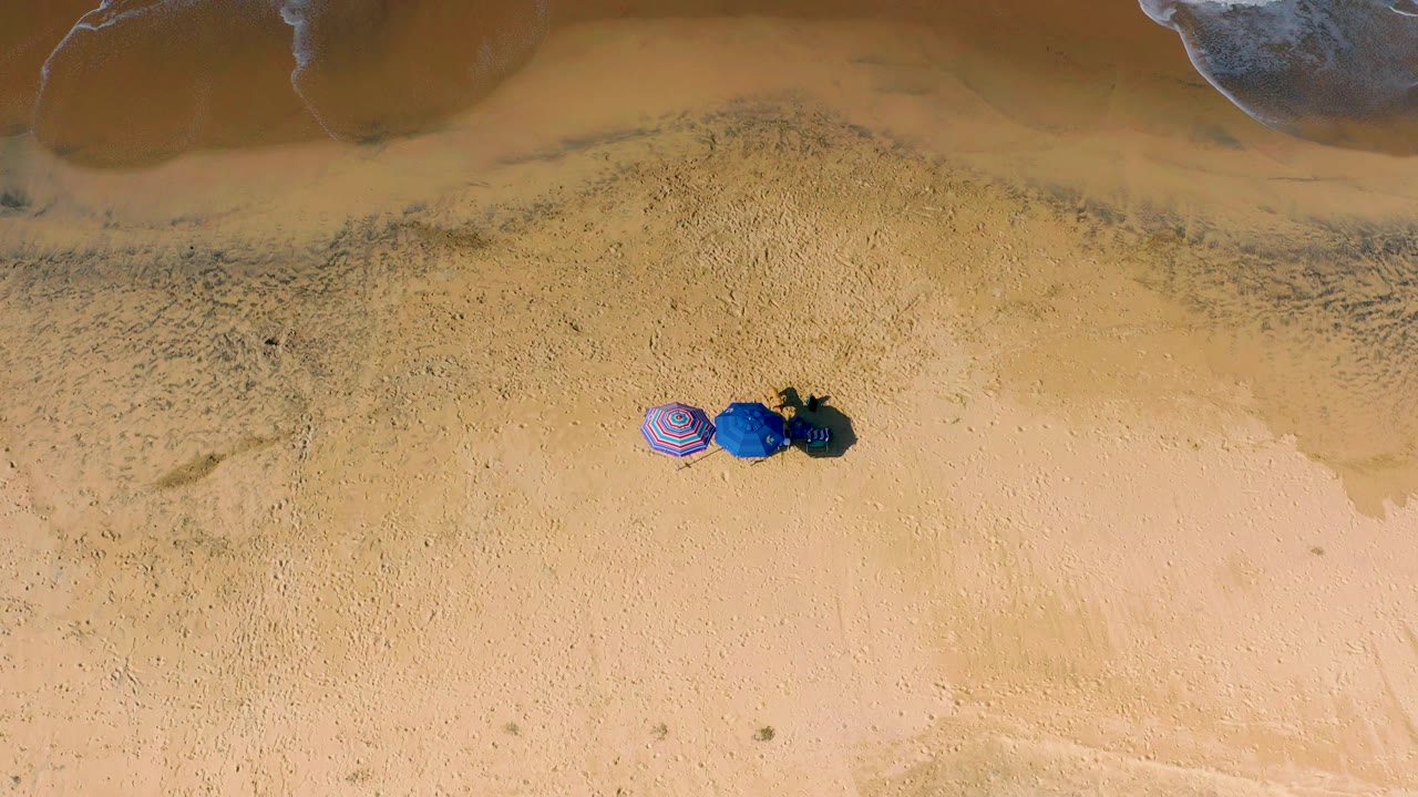 Straight-down Cerritos beach view with the beach items centered low in frame, darker wet sand above them, and pale surf just outside the upper edge, with no visible people.