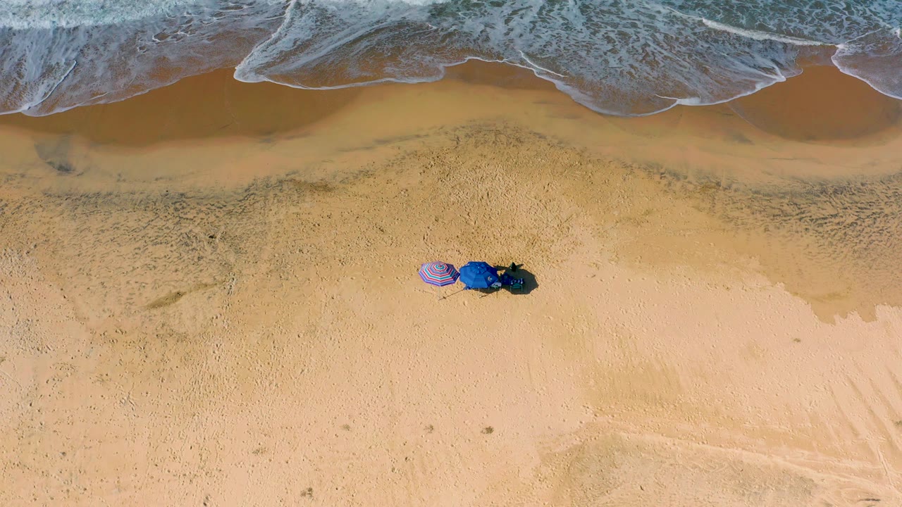 Top-down surf and sand with umbrellas near the shoreline