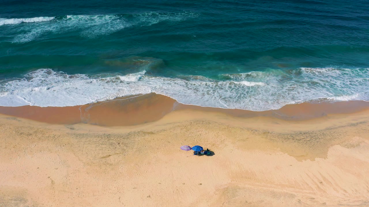 The Cerritos shoreline remains centered in a vertical overhead composition, with textured blue water, white surf, open tan sand, and no visible people.