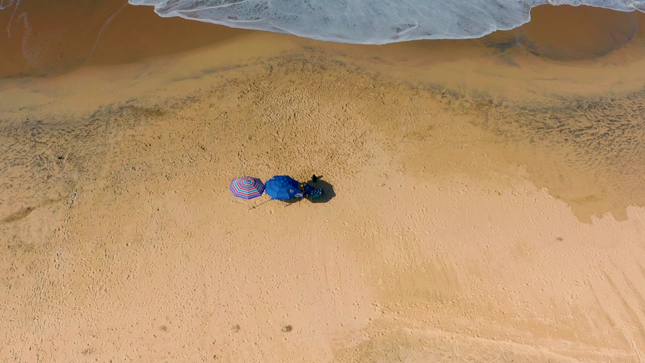 Overhead beach view with three umbrellas on sand below the surf line.