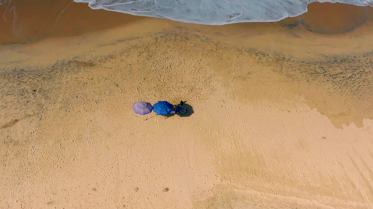 Aerial frame of Cerritos beach sand with the umbrella cluster slightly left of center, darker wet sand above, and no visible people.
