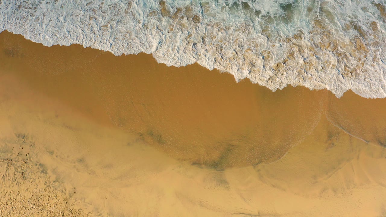 Overhead view of white surf reaching a golden sandy beach in Cerritos, Baja California Sur, with no visible people.
