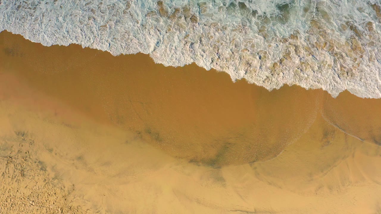 A foamy wave edge spreads farther down the wet golden sand at Cerritos, Baja California Sur, with no visible people.