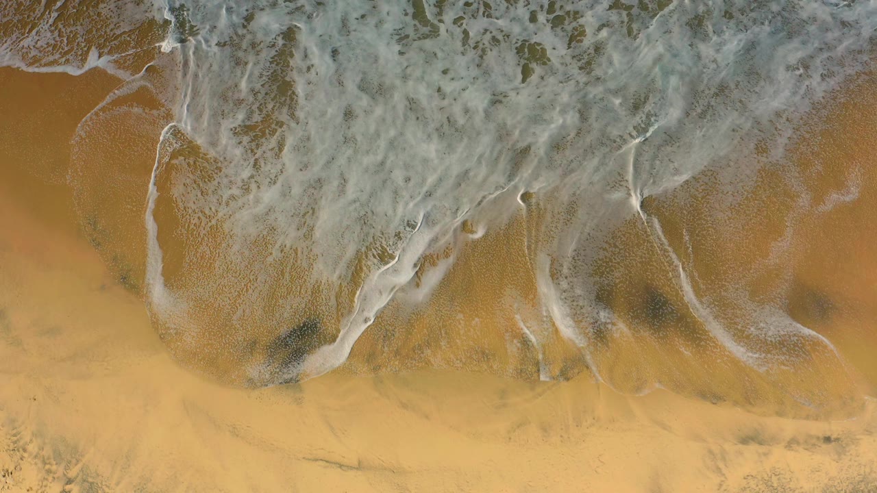 A thicker band of white surf covers the top of the frame while open Cerritos sand remains visible below, with no visible people.