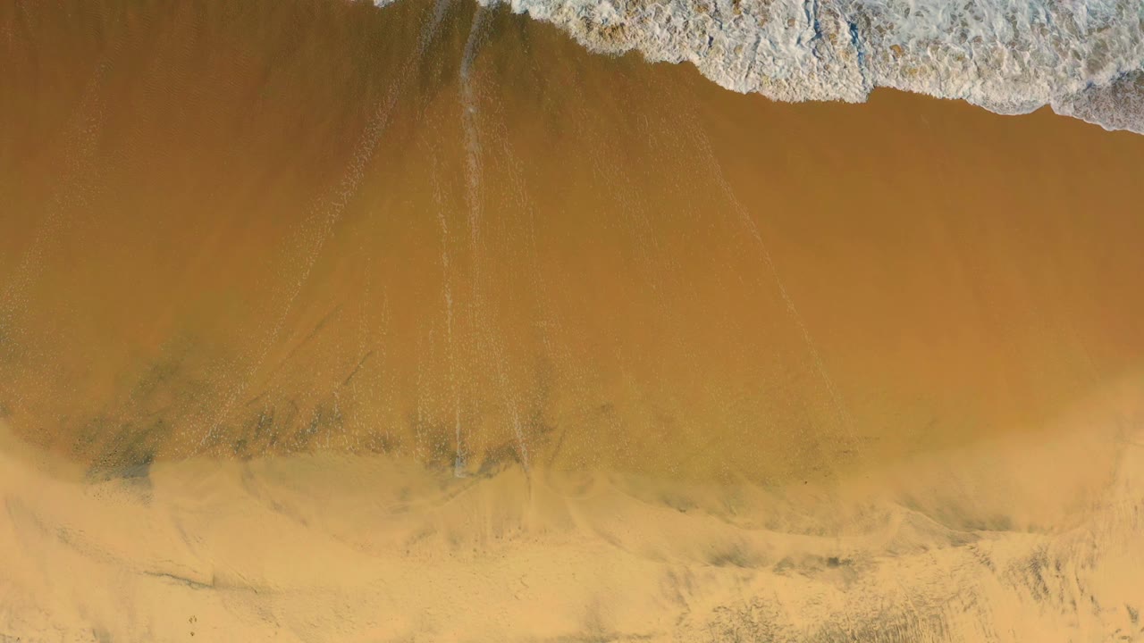 White wave foam runs along the top of the frame above smooth wet sand in Cerritos, Baja California Sur, with no visible people.