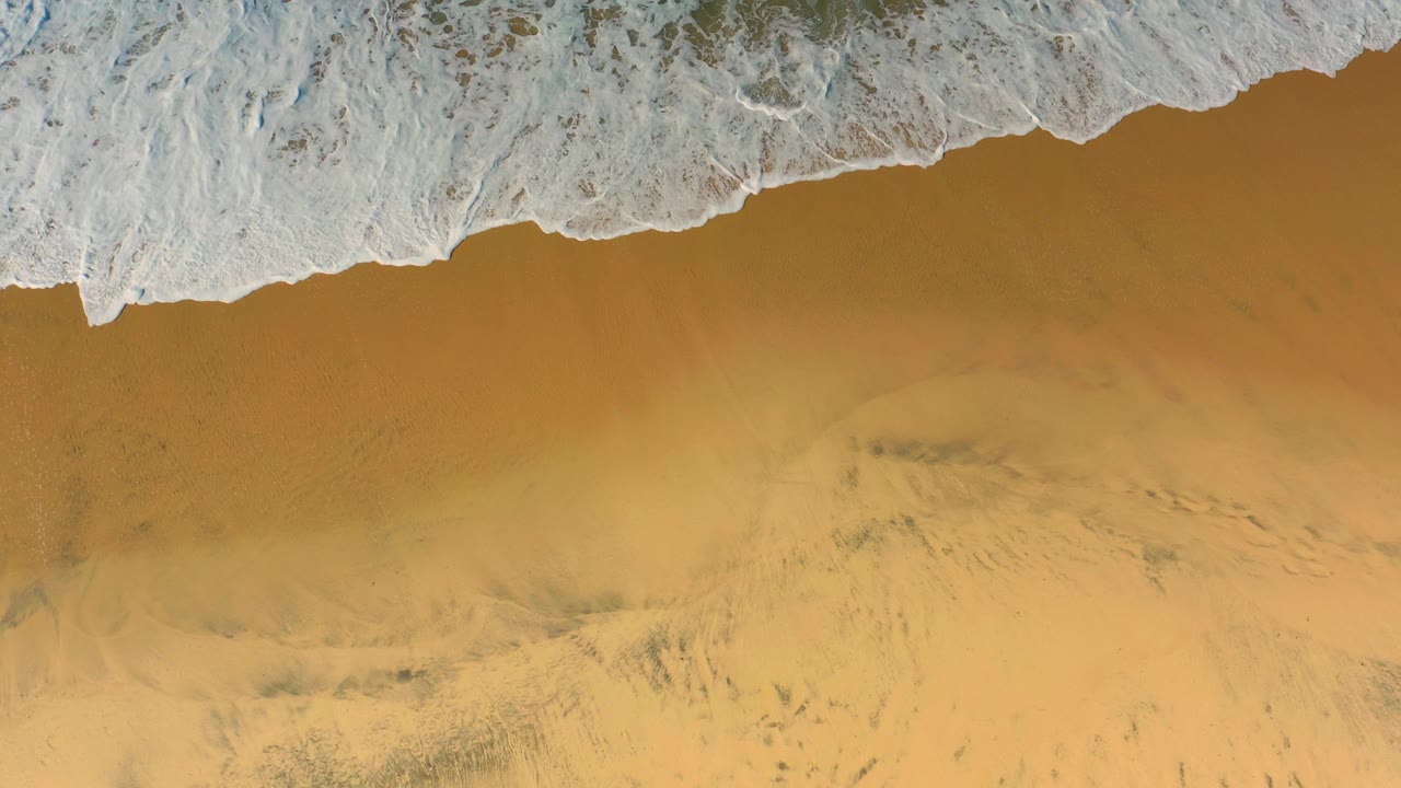 White surf curls diagonally across the top of the overhead Cerritos beach view, leaving open wet sand below and no visible people.