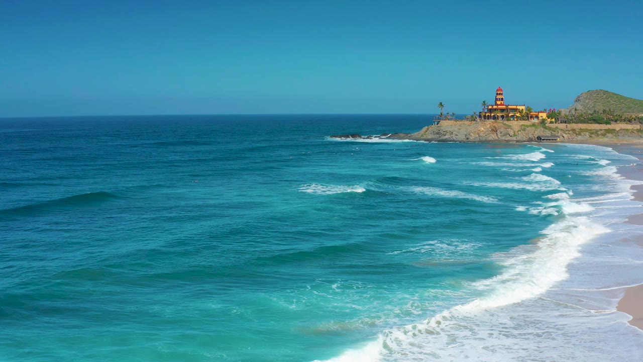 At 0:01, the surf line curves through the right side of the Cerritos beach view while turquoise shallows lead back to the bluff and distant buildings, with no visible people.