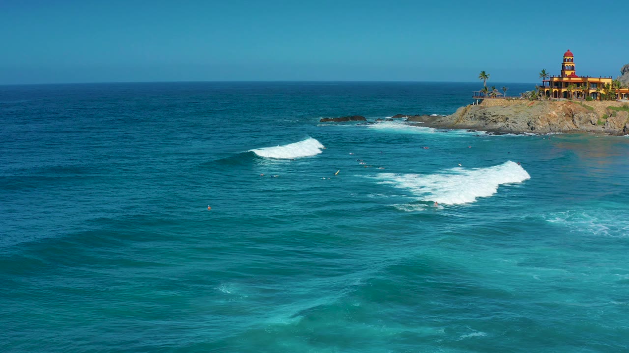 At 0:03 in Cerritos, Baja California Sur, turquoise water occupies the lower frame while two white surf lines cut across the midground below the rocky point, with no visible people.