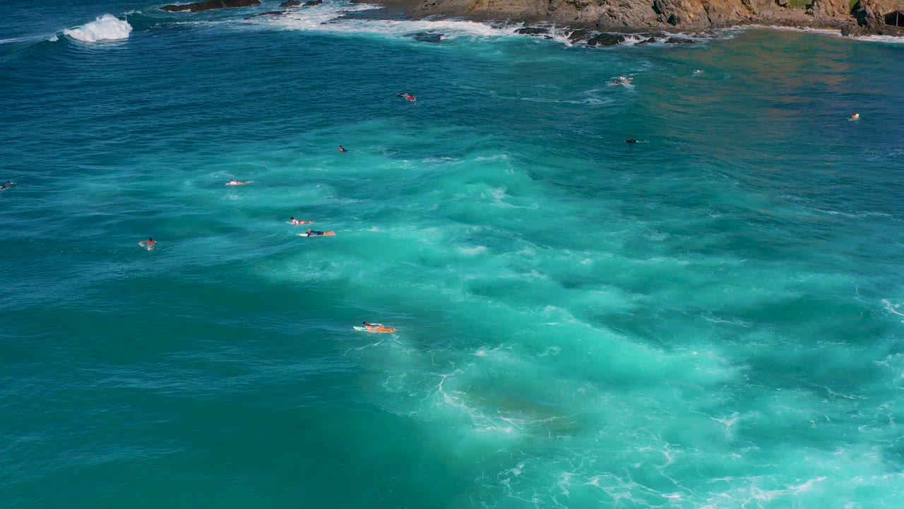 Aerial view over Cerritos, Baja California Sur, with turquoise water, tiny board riders, white surf, and rocky shoreline along the top edge.