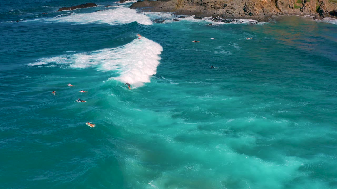 Large white surf line breaks diagonally over turquoise water near the coast.