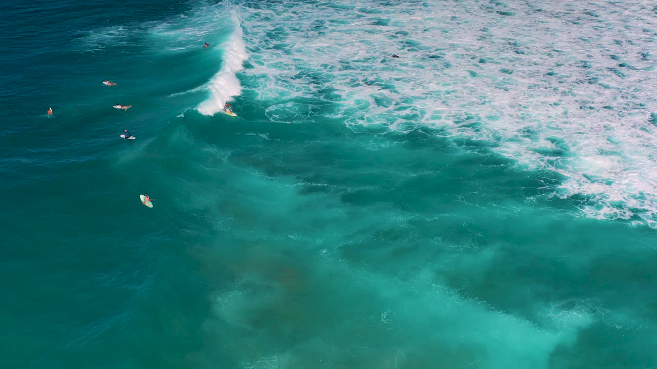 The breaking wave advances across the right side of the Cerritos ocean frame while the riding surfer stays near the whitewater and other surfers sit offshore.